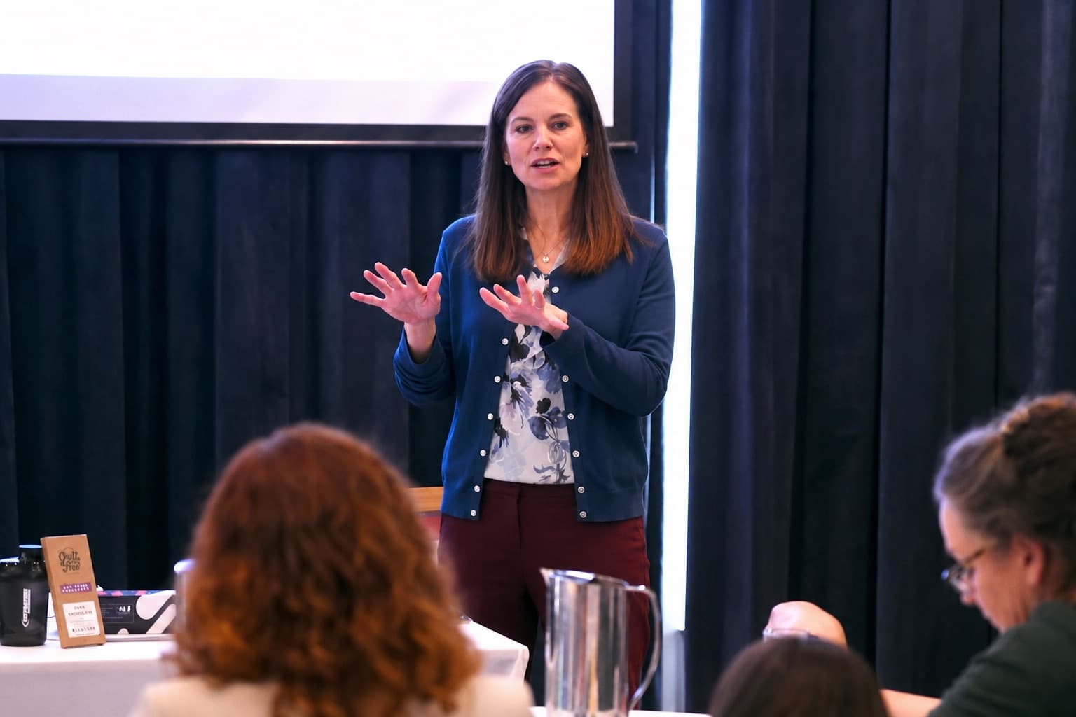 Dr Jonie Girouard speaking to a seated audience at a live seminar, hands gesturing to explain a concept